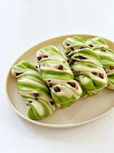Green and white swirled cookies with chocolate chips on a beige plate.