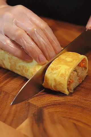 Person cutting a rolled omelette with a knife on a wooden surface
