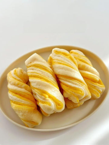 Three twisted bread rolls on a beige plate with a white background