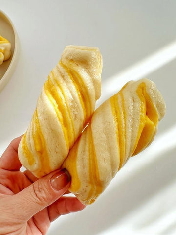 Hand holding a twisted bread roll with yellow filling on a white background
