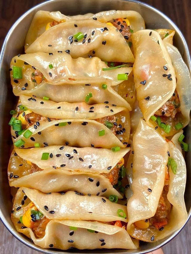 Baked potstickers in a metal dish with sesame seeds and green onions on top.