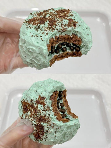 Green mint chocolate chip ice cream ball held by a hand on a white background