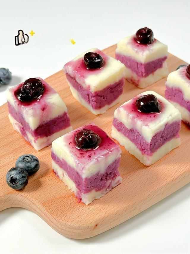 Squares of purple and white dessert with blueberries on a wooden board