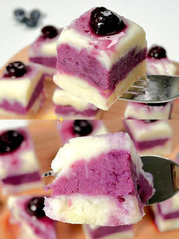 Slices of purple and white dessert with blueberries on a wooden board.