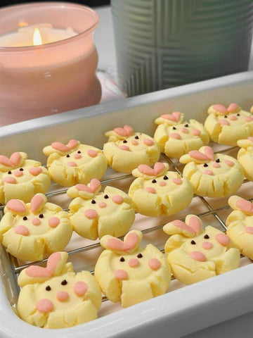 Decorative cookies shaped like bunnies on a cooling rack with a candle in the background.