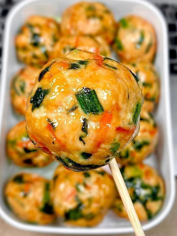 Close-up of a skewer with a meatball and a tray of more meatballs in the background.