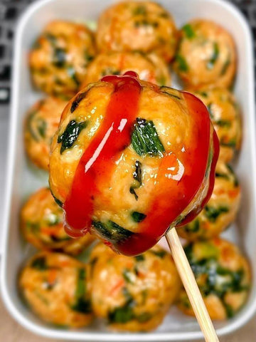 Dumpling on a stick with red sauce over a tray of similar dumplings.