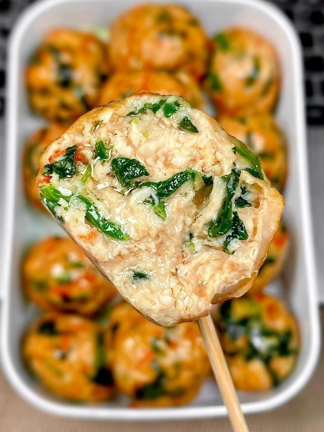 Close-up of a meatball skewer with spinach on a white plate filled with more meatballs.
