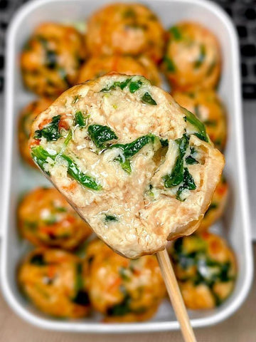 Close-up of a meatball skewer with spinach on a white plate filled with more meatballs.