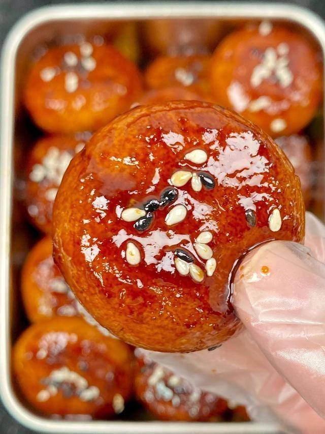 Close-up of a glazed dessert ball with sesame seeds, held by a gloved hand.