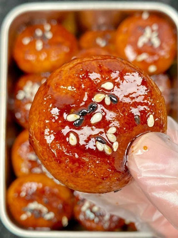Close-up of a glazed dessert ball with sesame seeds, held by a gloved hand.