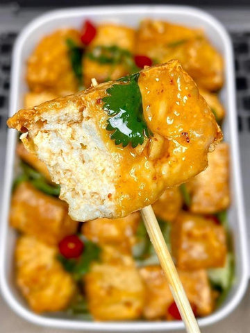 Fried tofu cube on a stick with a blurred container of more tofu in the background