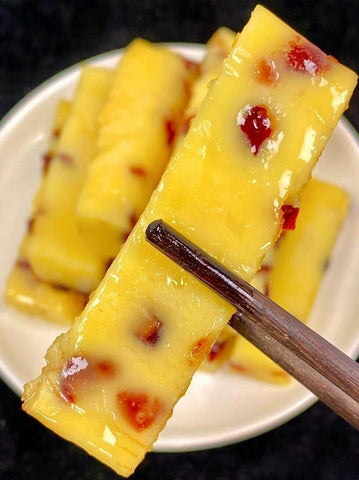 Yellow dessert bars with red seeds on a white plate with chopsticks