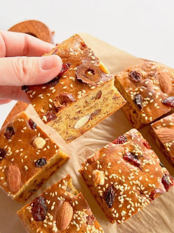 Hand holding a piece of baked snack with nuts and dried fruits on a wooden surface