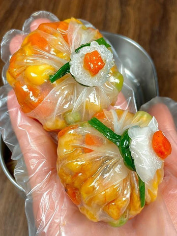 Three colorful dumplings wrapped in clear plastic on a metal tray.