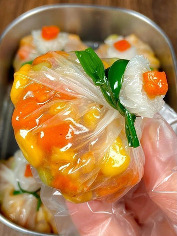 Close-up of a dumpling with vegetables and a green leaf, held by a gloved hand.