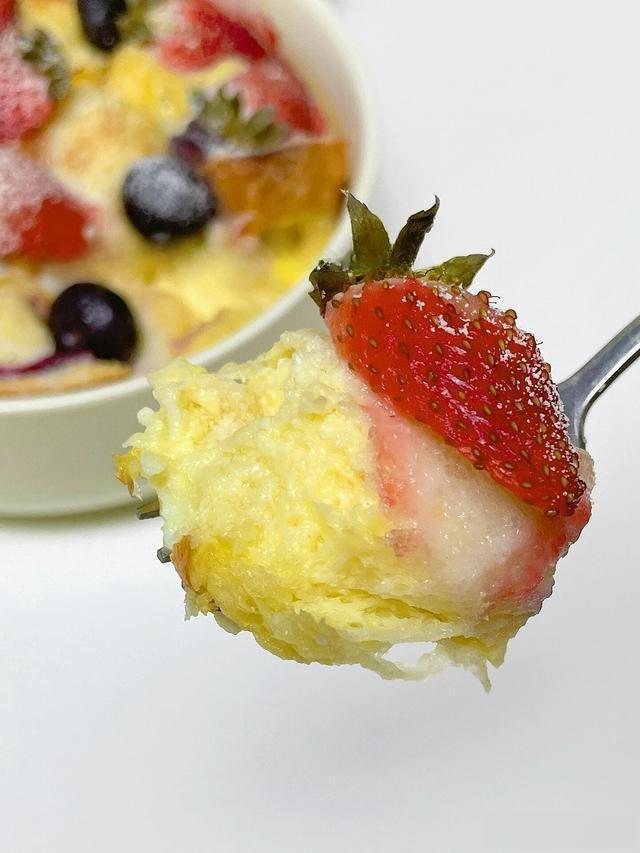 Spoonful of dessert with strawberry and yellow cake-like topping on a white background