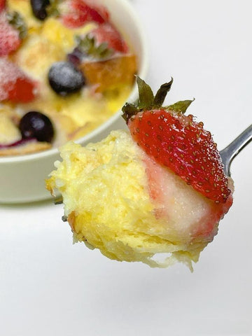 Spoonful of dessert with strawberry and yellow cake-like topping on a white background