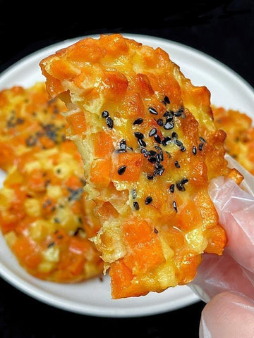 Crispy orange snack with black sesame seeds on a white plate