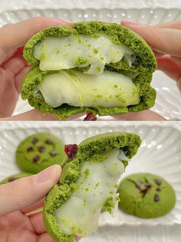 Green matcha cookie with white cream filling held by a hand, with another cookie in the background.